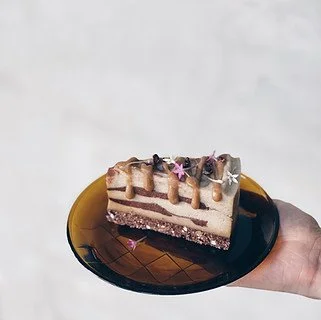 A piece of layered chocolate and vanilla cake with drip icing and pink decorative stars on a black plate.