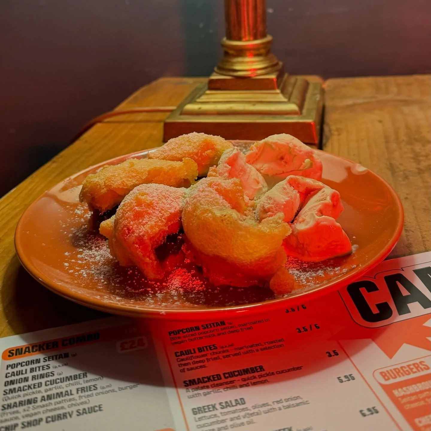 Plate of fried food with a dusting of powdered sugar on a table at a restaurant or cafe.