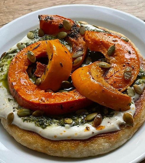 A pizza with roasted pumpkins, seeds, and herbs on a white plate.