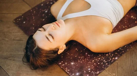 Woman lying on a yoga mat with eyes closed, relaxing.
