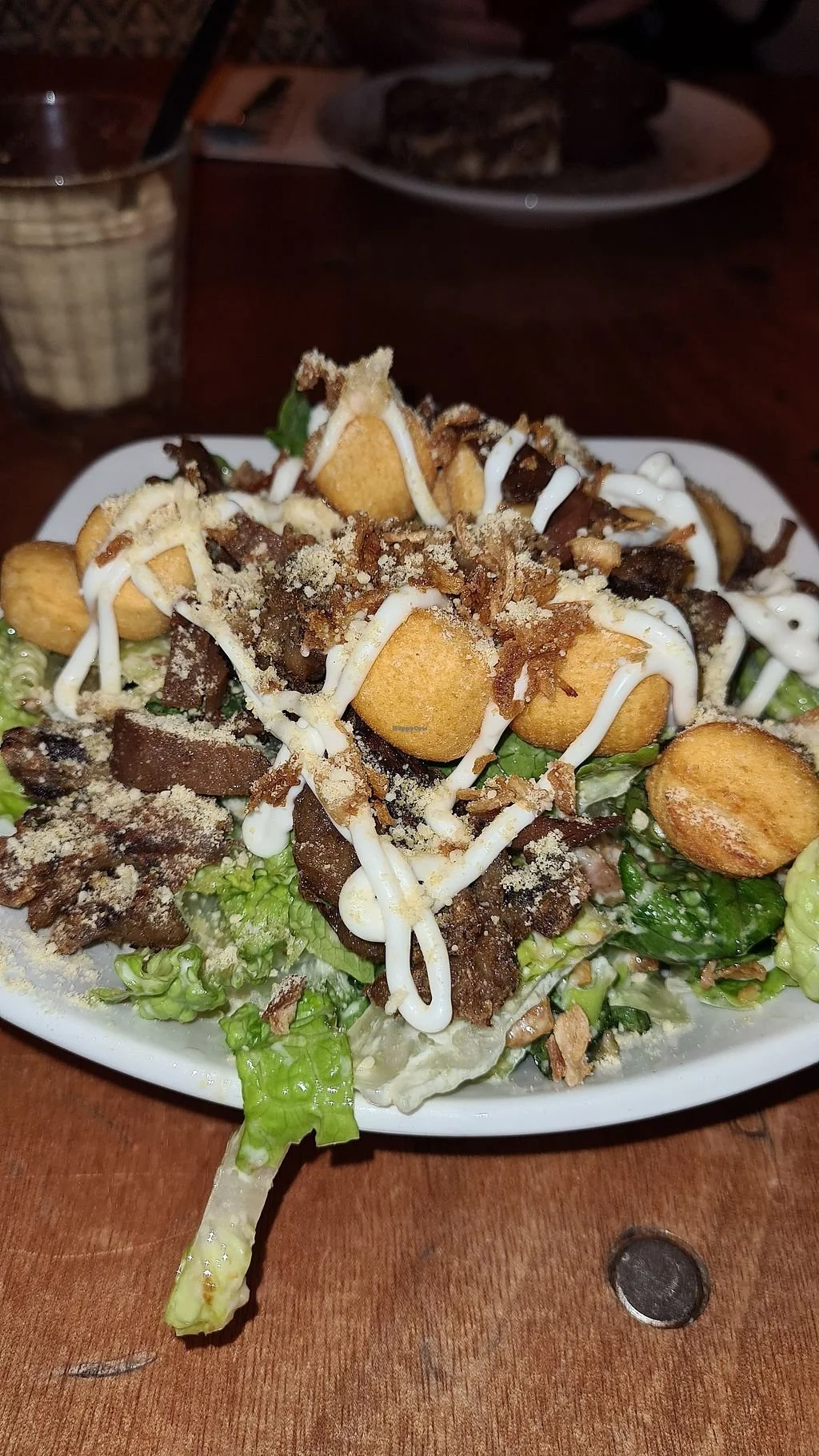 A salad with lettuce, croutons, shredded cheese, sliced mushrooms, and drizzled with white dressing, served on a white plate.