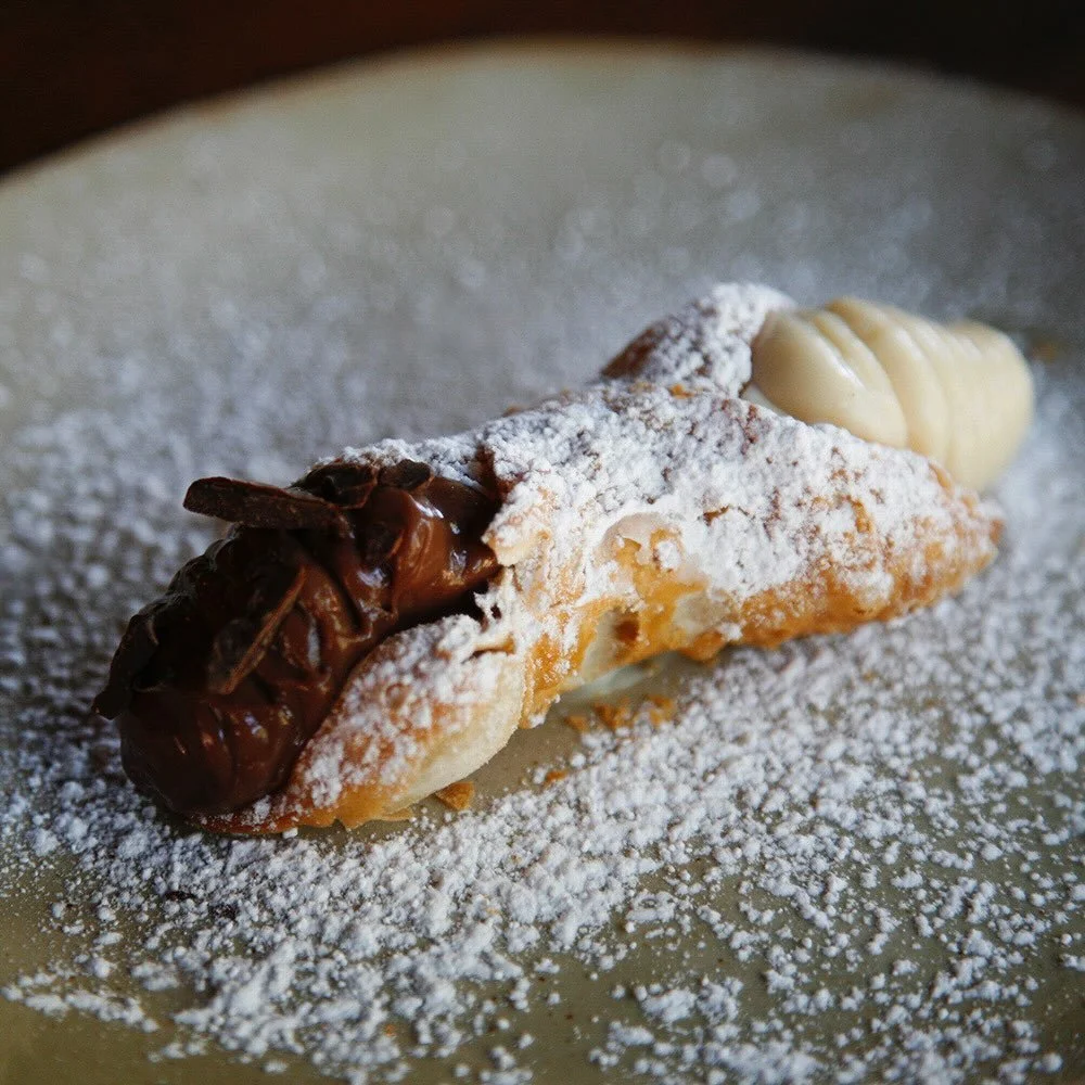 A cannoli filled with chocolate and white cream, dusted with powdered sugar on a plate.