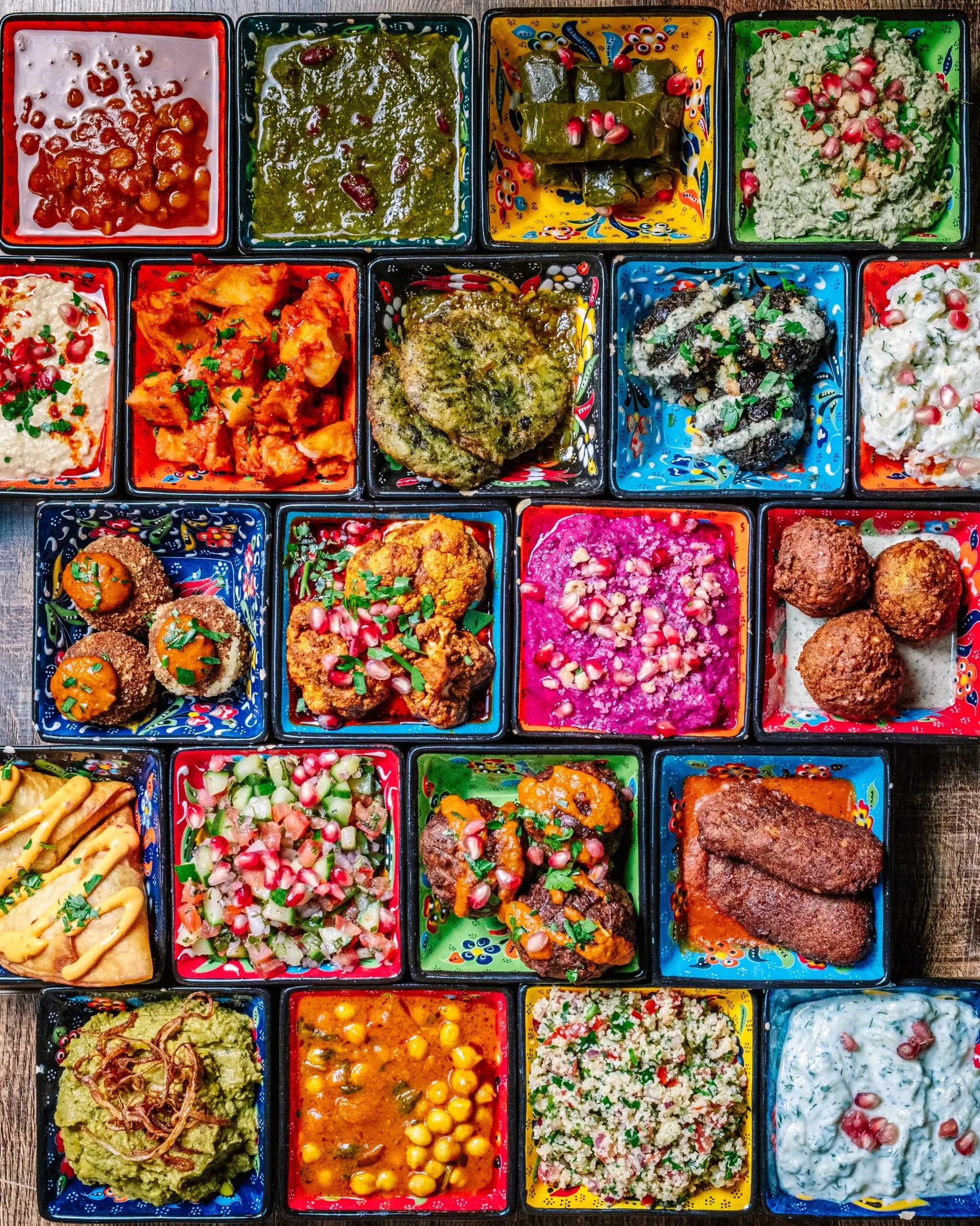 Colorful Mexican food dishes in small bowls on a tray, including guacamole, salsas, salads, and rice, decorated with pomegranate seeds and herbs.