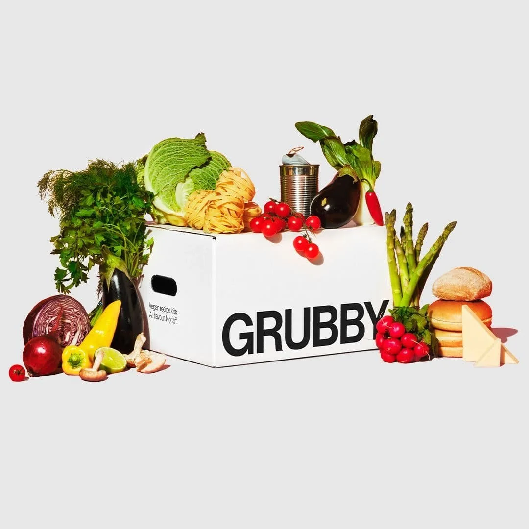 Assorted fresh vegetables and cheese around a white box labeled 'GRUBBY' on a white background.