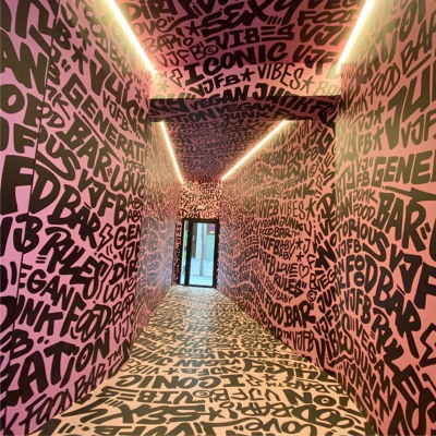 Hallway with pink walls covered in black graffiti-style text, illuminated by strip lights, leading to a door at the end.
