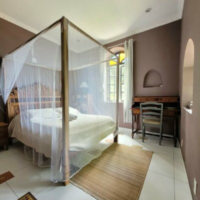 A cozy bedroom with a four-poster bed surrounded by a white canopy, a wooden desk with a chair, a window with curtains, and a brown accent wall.