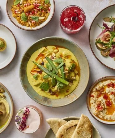 Assorted Indian dishes and drinks on a table, including curry with green beans, salad, raita, and a beverage.