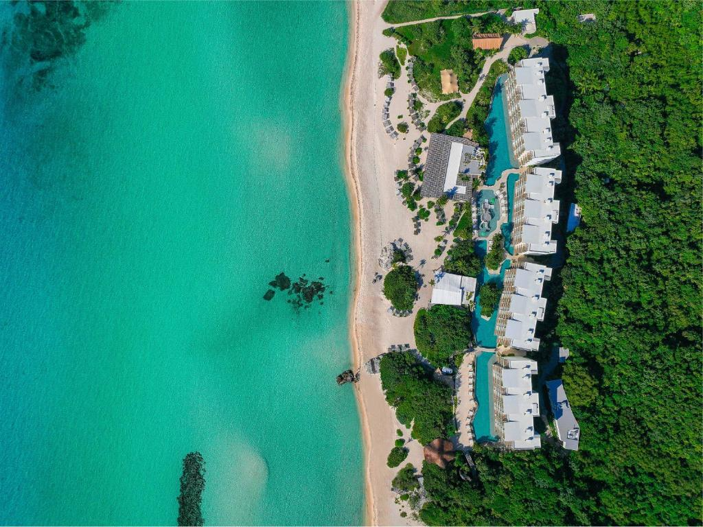 Aerial view of a beachfront resort with multiple white buildings, a swimming pool, beach, and lush greenery along the coastline.