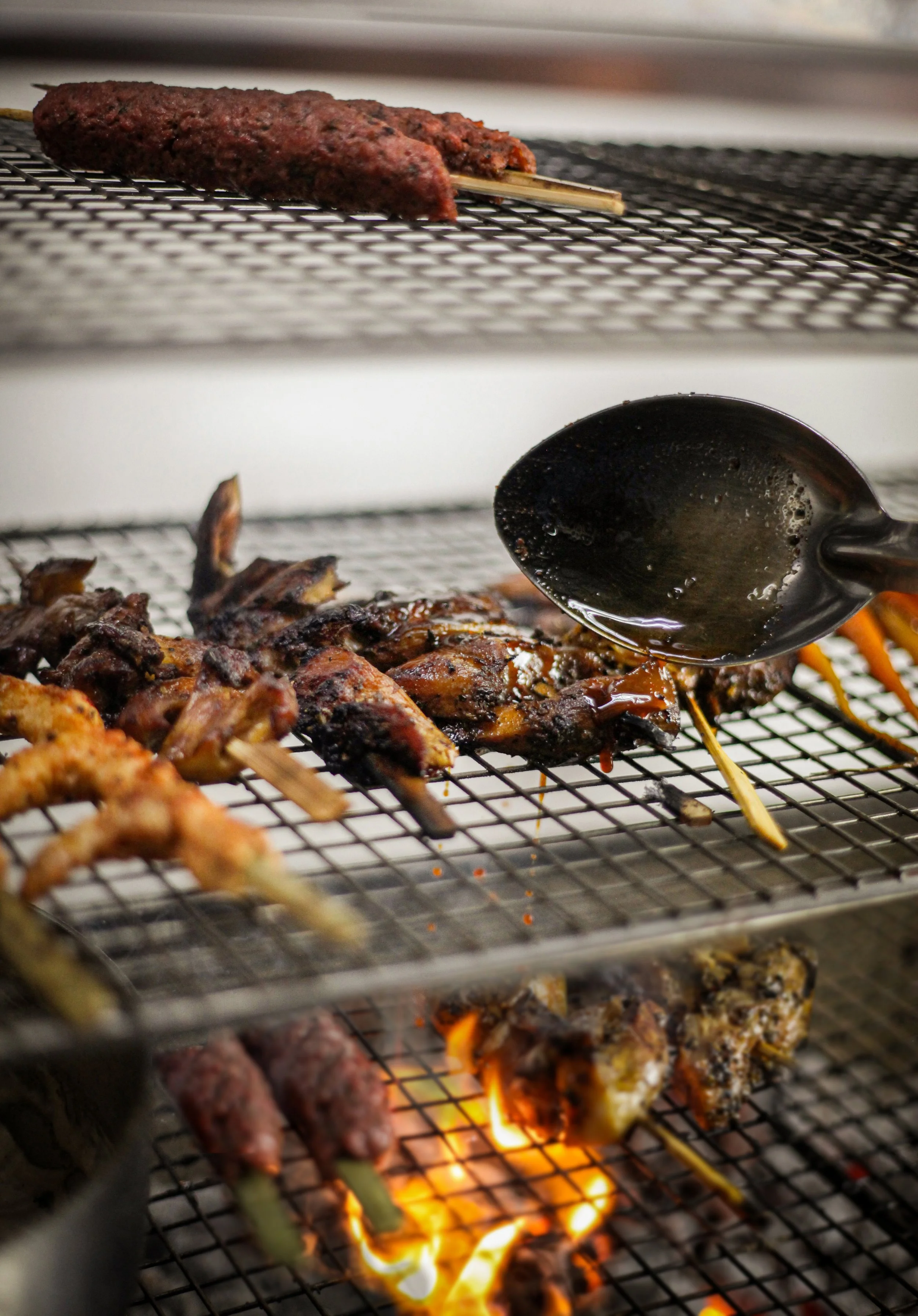 Grilled meat skewers on a grill with open flames and a spatula.