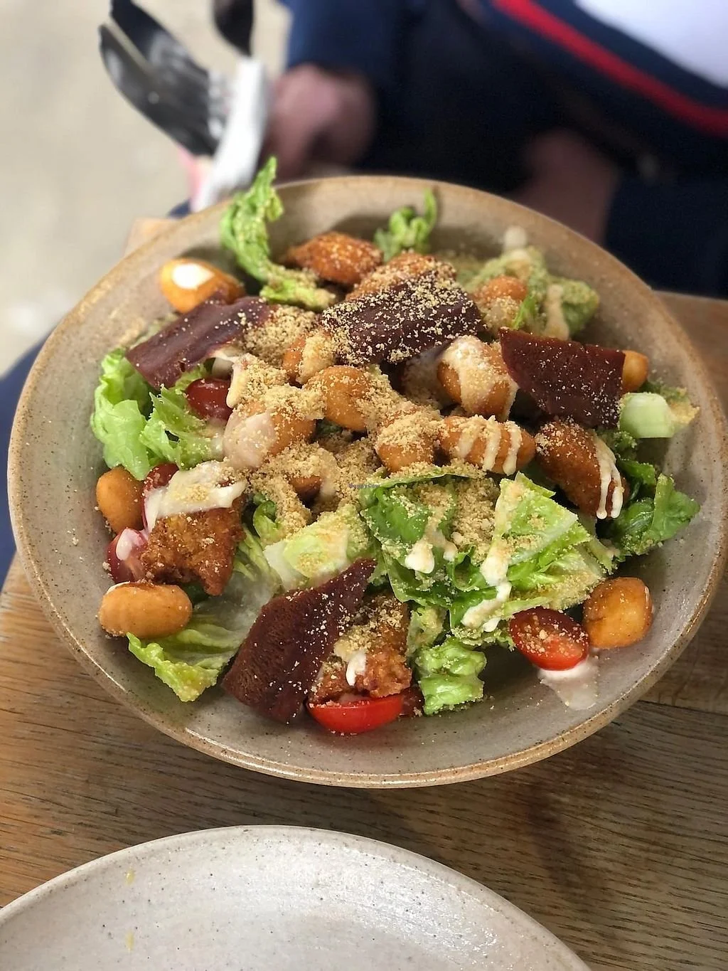 A bowl of Asian-style salad with lettuce, cherry tomatoes, fried tofu, peanuts, sliced beef, green vegetables, shredded cheese, and sprinkled crushed peanuts on top.