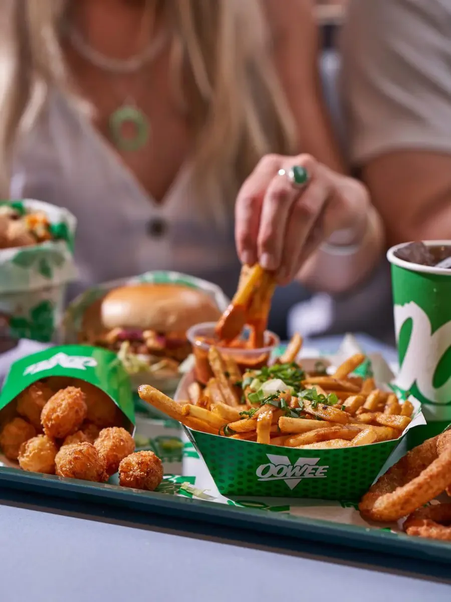 Person eating French fries with a side of chicken nuggets and a burger at a fast food restaurant.