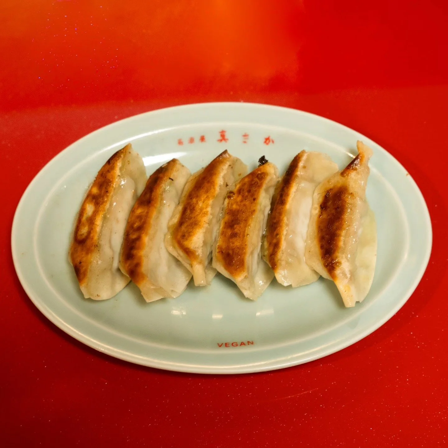 Plate of six fried vegan dumplings on a white plate with red accents, placed on a red table.