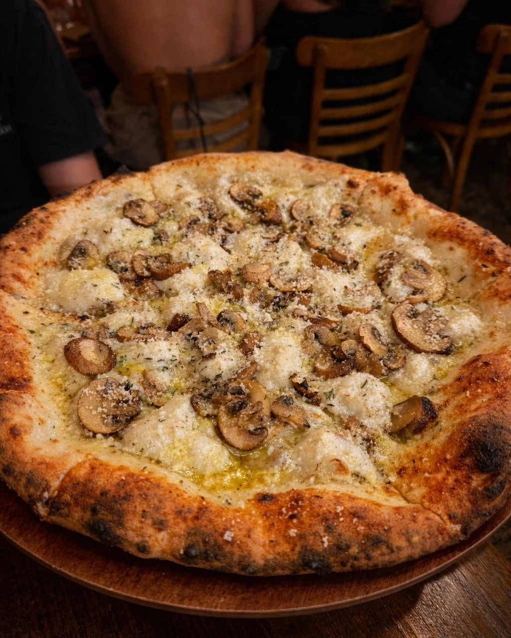 A mushroom and cheese pizza with a golden crust served on a wooden plate in a restaurant setting.