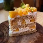 A slice of layered mango cake with yellow mango slices and whipped cream on top, on a wooden serving board.