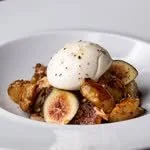 A dessert with figs, fried dough, and a scoop of ice cream topped with a sprinkle of black pepper.