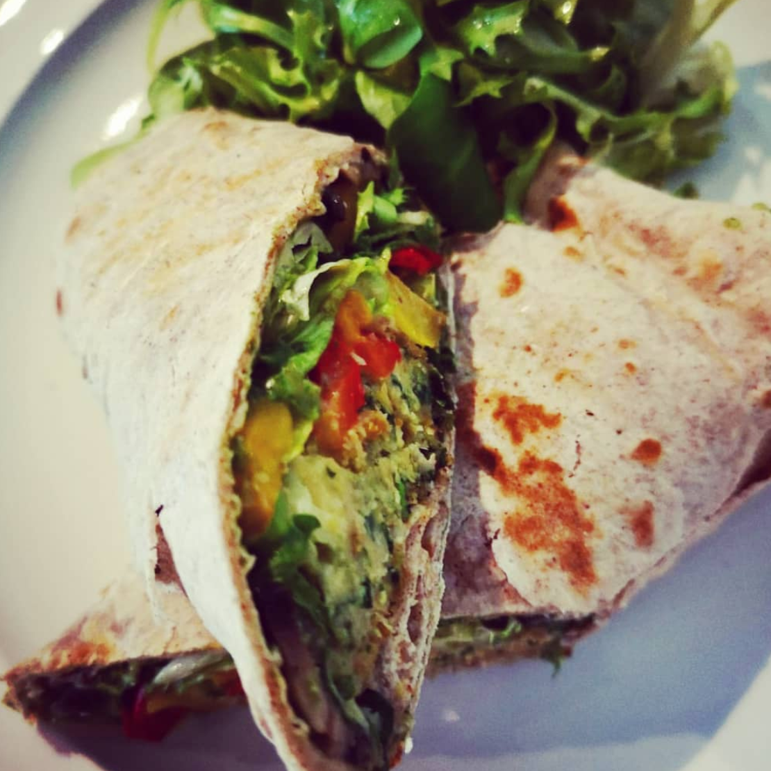 A close-up of a veggie wrap cut in half, showing lettuce, tomatoes, and other vegetables inside a tortilla, with a side of salad.