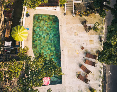 A swimming pool area with a yellow umbrella, four lounge chairs, a pink pool float, and surrounding trees and plants.