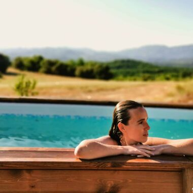 Woman relaxing in an outdoor swimming pool with a scenic landscape in the background.