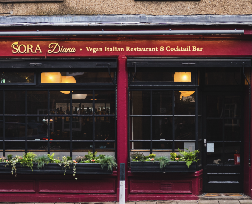 Exterior of vegan Italian restaurant and cocktail bar named Sora Diana with dark red trim and large windowed front.