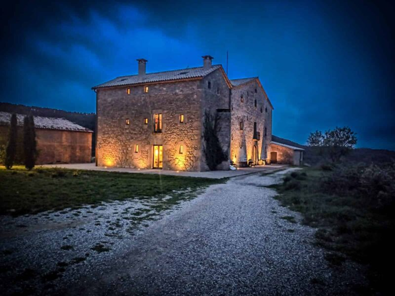 A stone building illuminated at night with outdoor lighting, surrounded by a gravel path and grassy area.