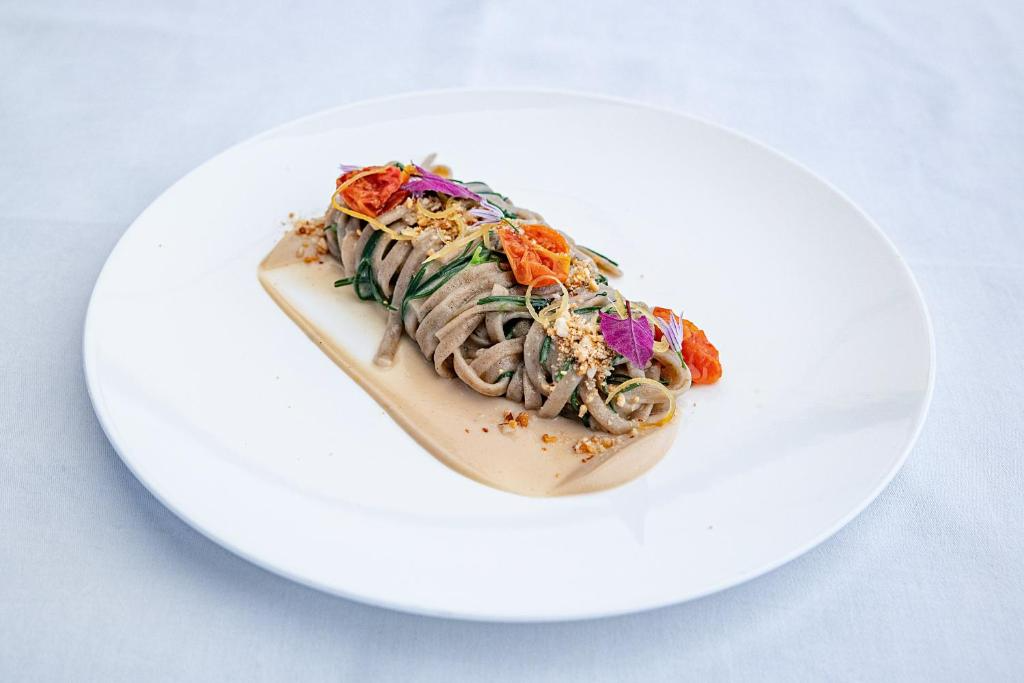 Plate of soba noodles with sauce, garnished with edible flowers and crushed nuts on a white plate.