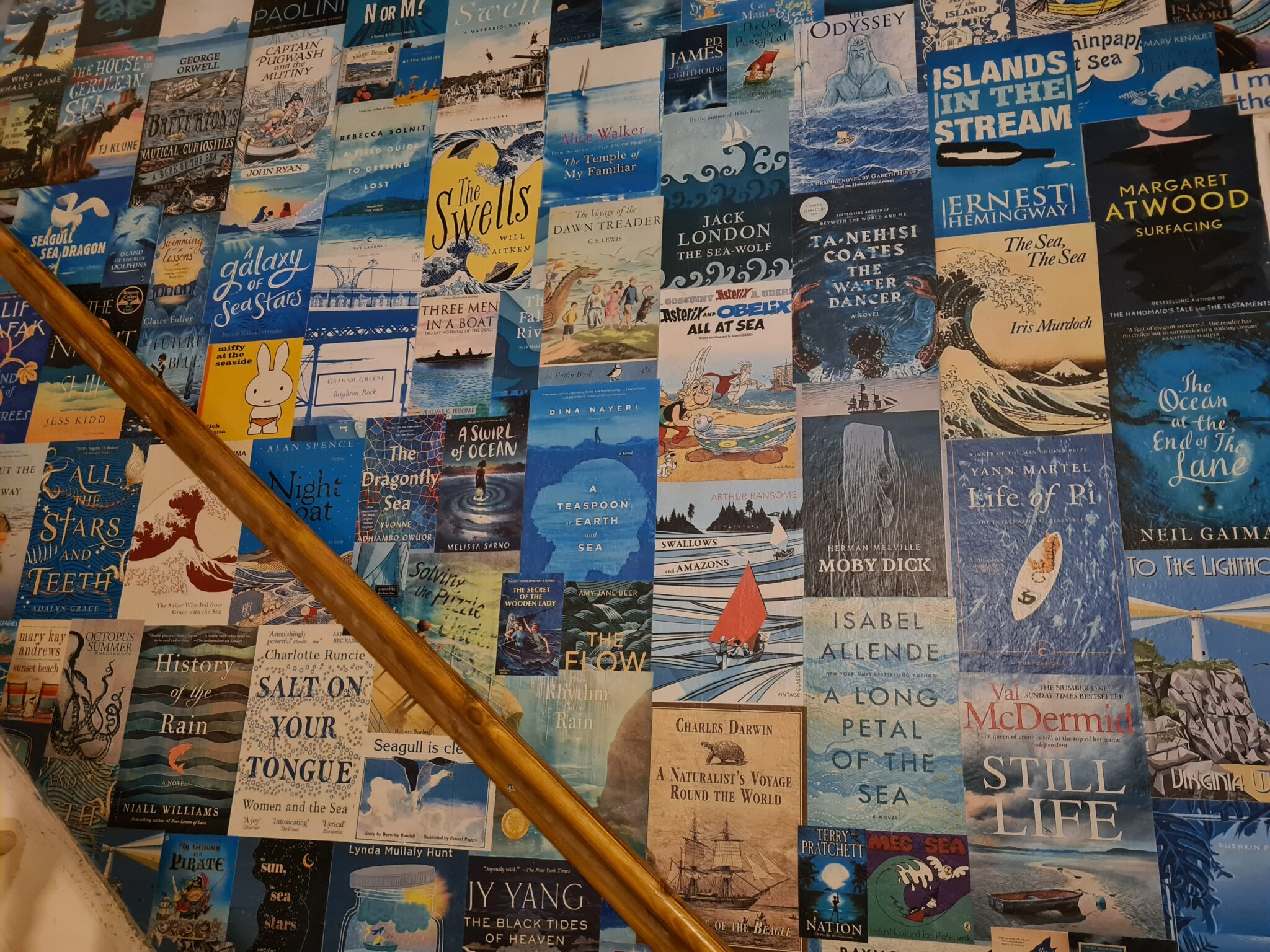 A wall decorated with numerous colorful books mainly about the sea, ocean, and sailing, arranged in a grid pattern.