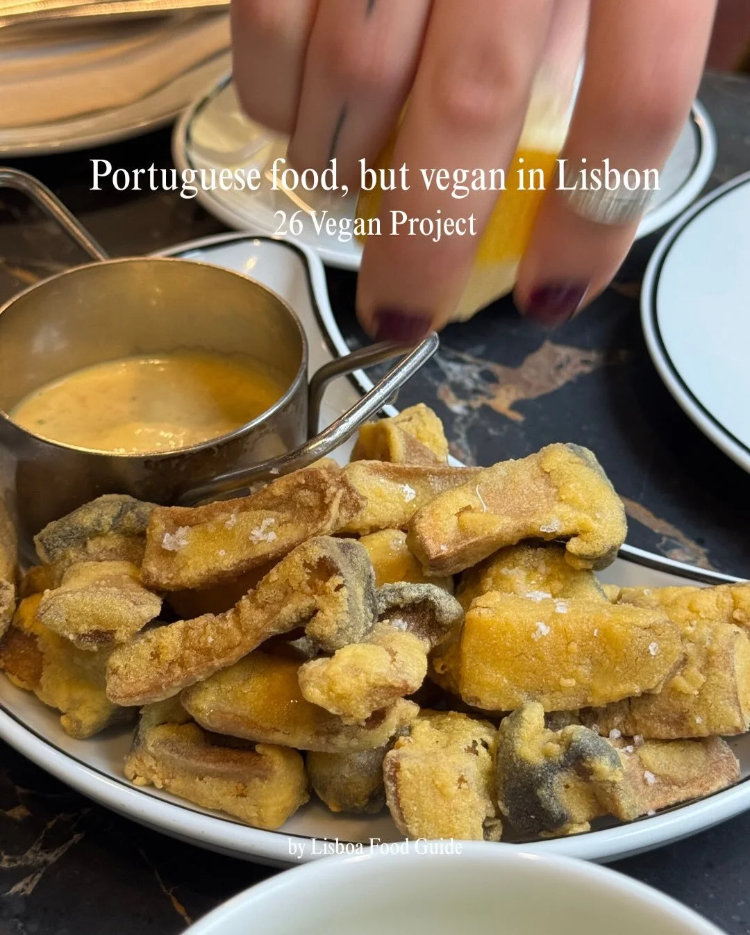Plate of fried vegan food with a dipping sauce in a small metal pot, set on a dark marble table with a person's hand reaching for the food.