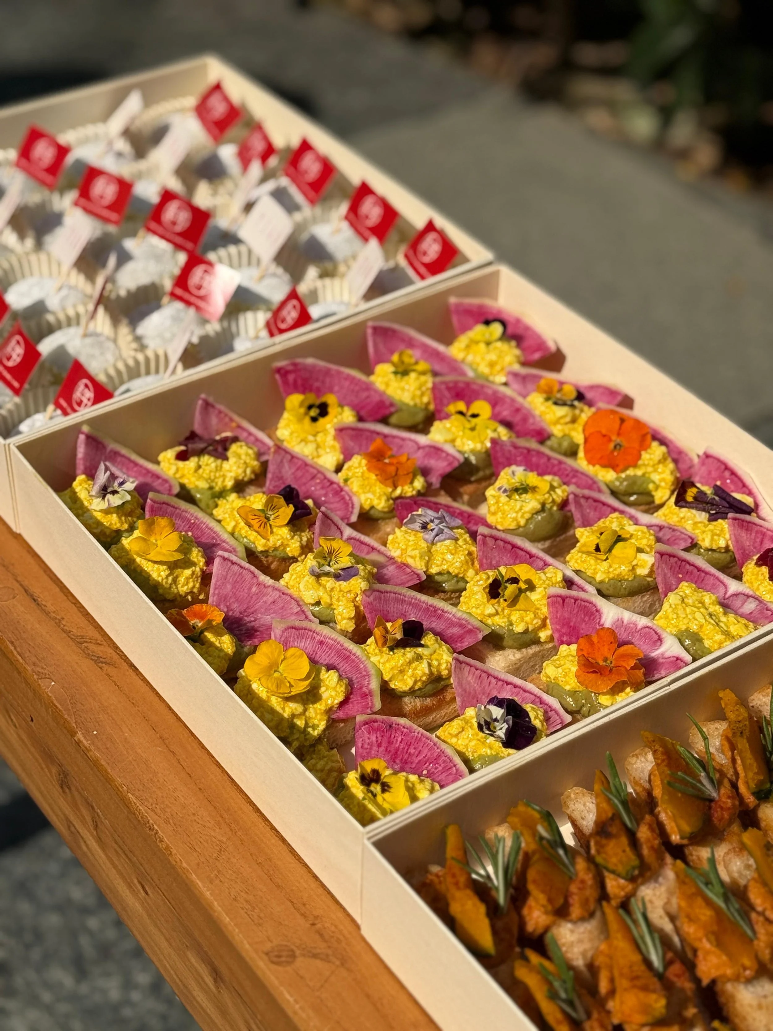 Colorful canapés topped with edible flowers on a wooden table.
