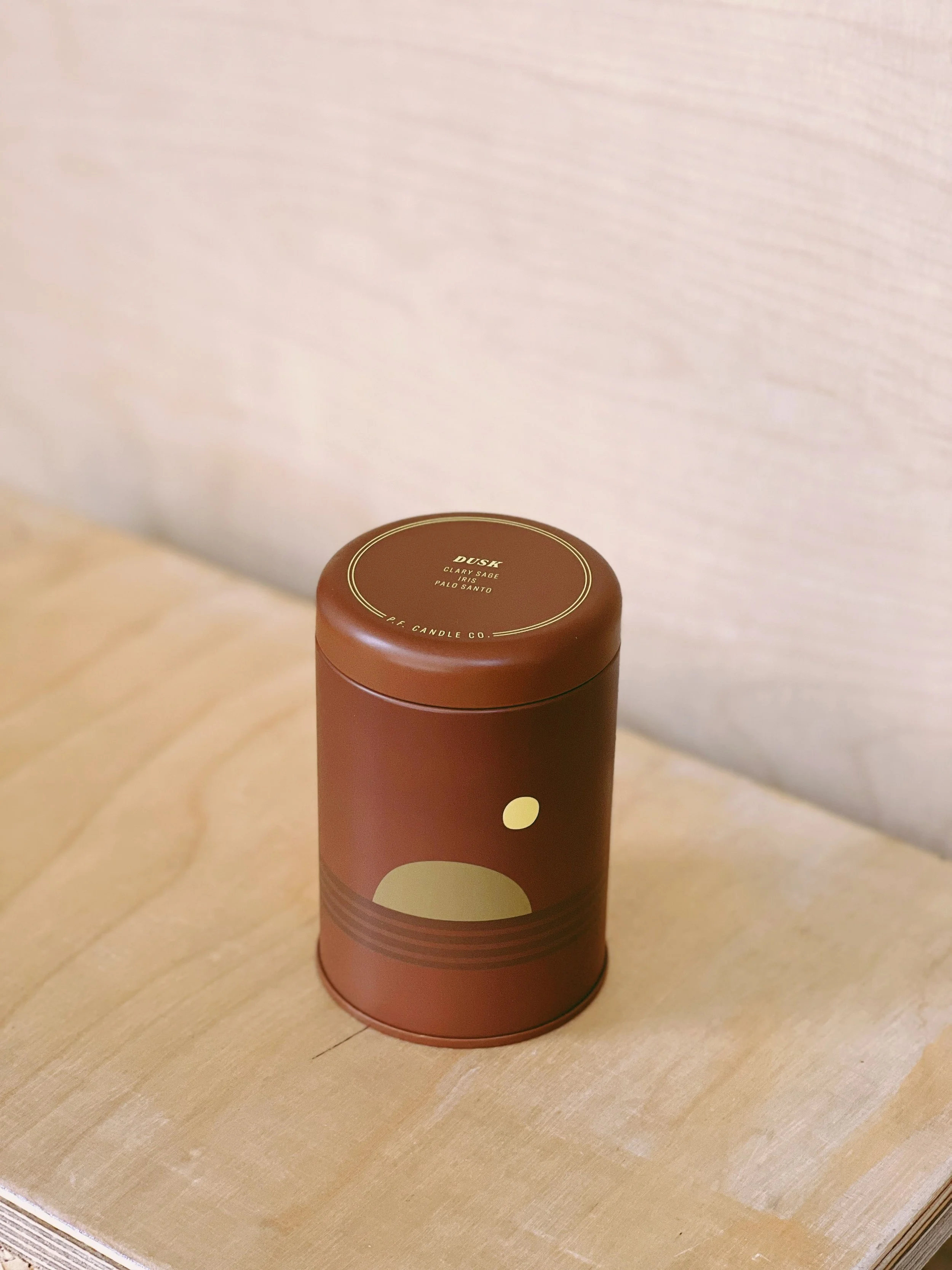 A cylindrical candle with a brown and beige design on a wooden surface