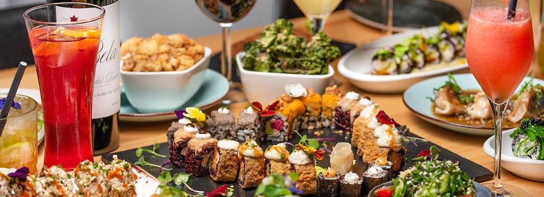 Assorted sushi rolls, salads, fried chicken, and beverages on a dining table.