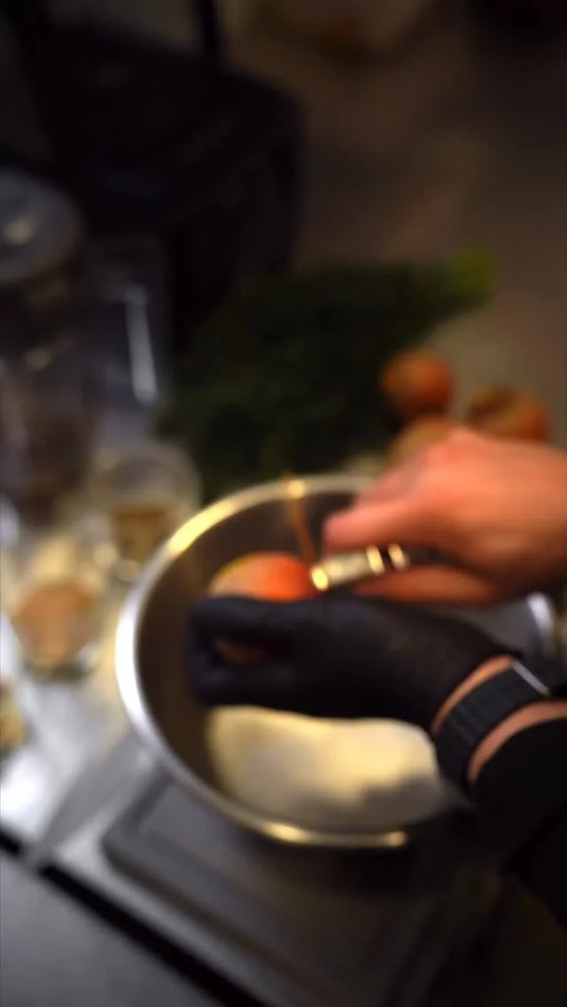 Person wearing a black glove preparing peaches in a stainless steel bowl on a stovetop, with green herbs in the background.