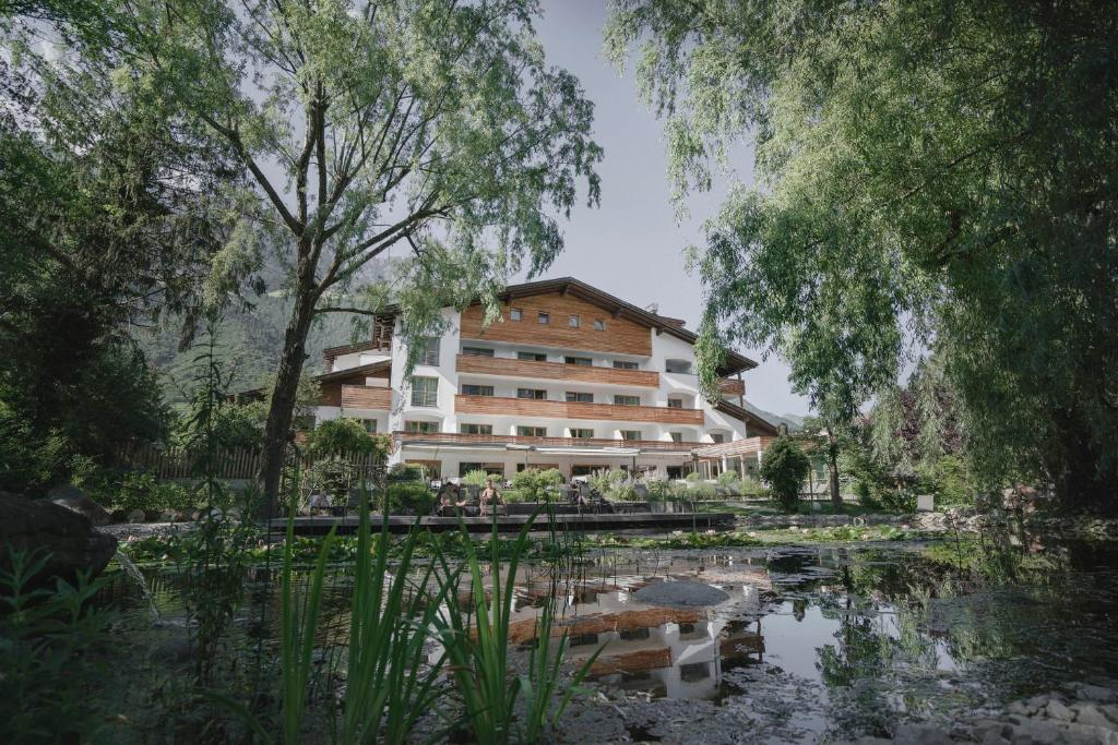 A multi-story building with wooden accents, surrounded by trees and a pond in the foreground.