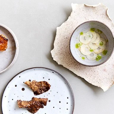 A white plate with fried chicken pieces, a small bowl with onion slices and green peas, and a partially visible fried chicken piece on a separate plate.
