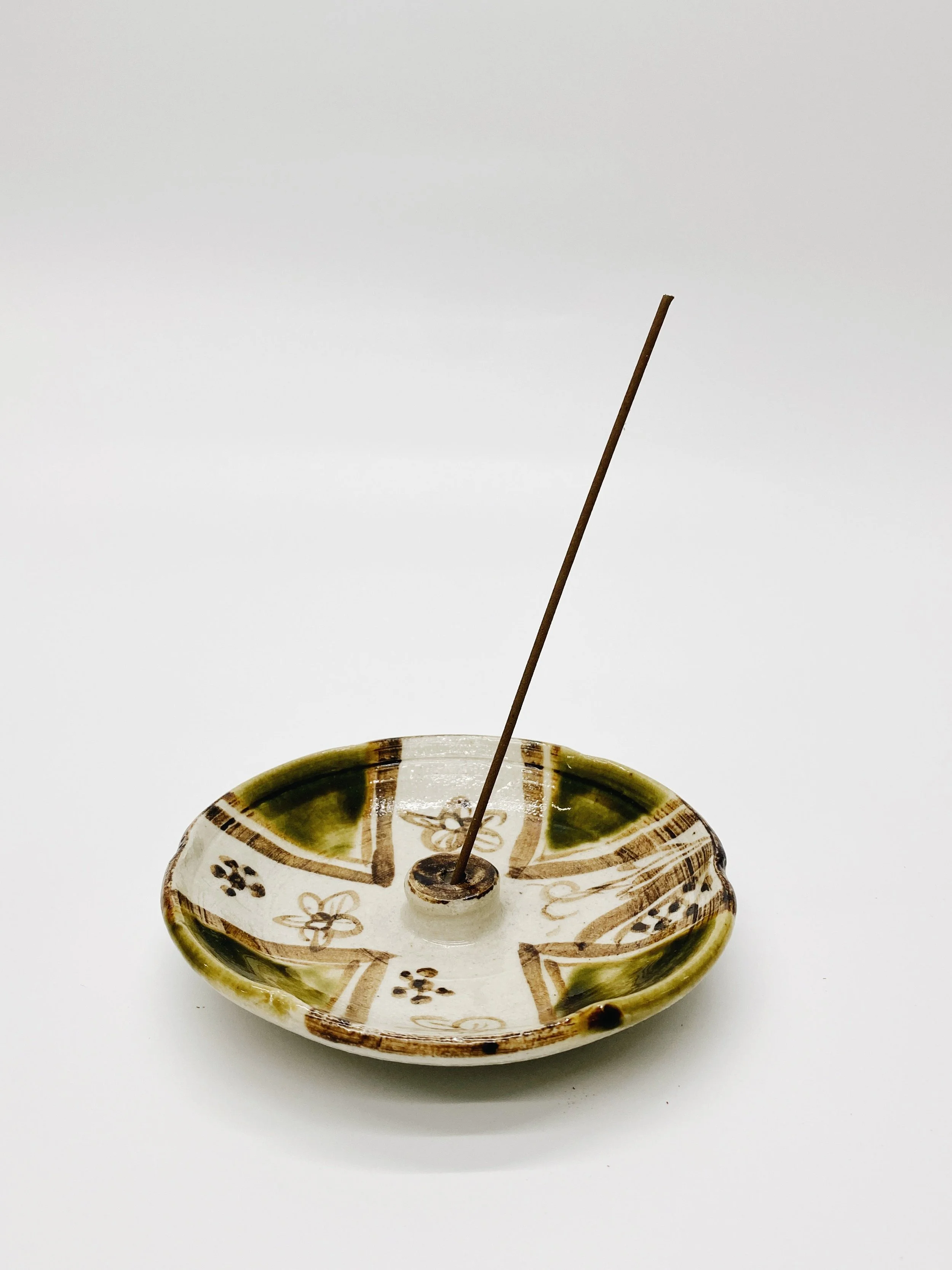 Ceramic incense holder with floral designs and a stick of incense inserted.