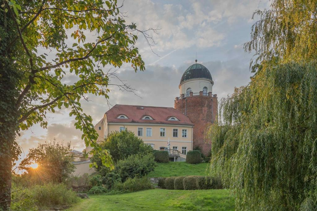 A scenic view of a historic building with a tower, surrounded by trees and greenery at sunset.