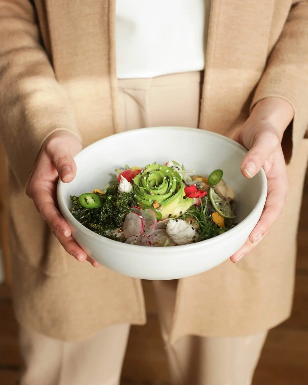 Person holding a white bowl filled with a colorful salad that includes sliced radishes, avocado rose, seaweed, and various vegetables.