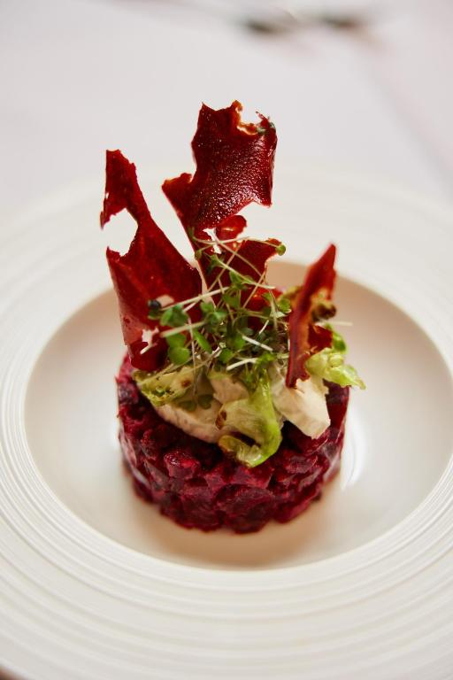 A gourmet dish featuring a round of beet tartare topped with microgreens, crispy beet chips, and lettuce on a white plate.