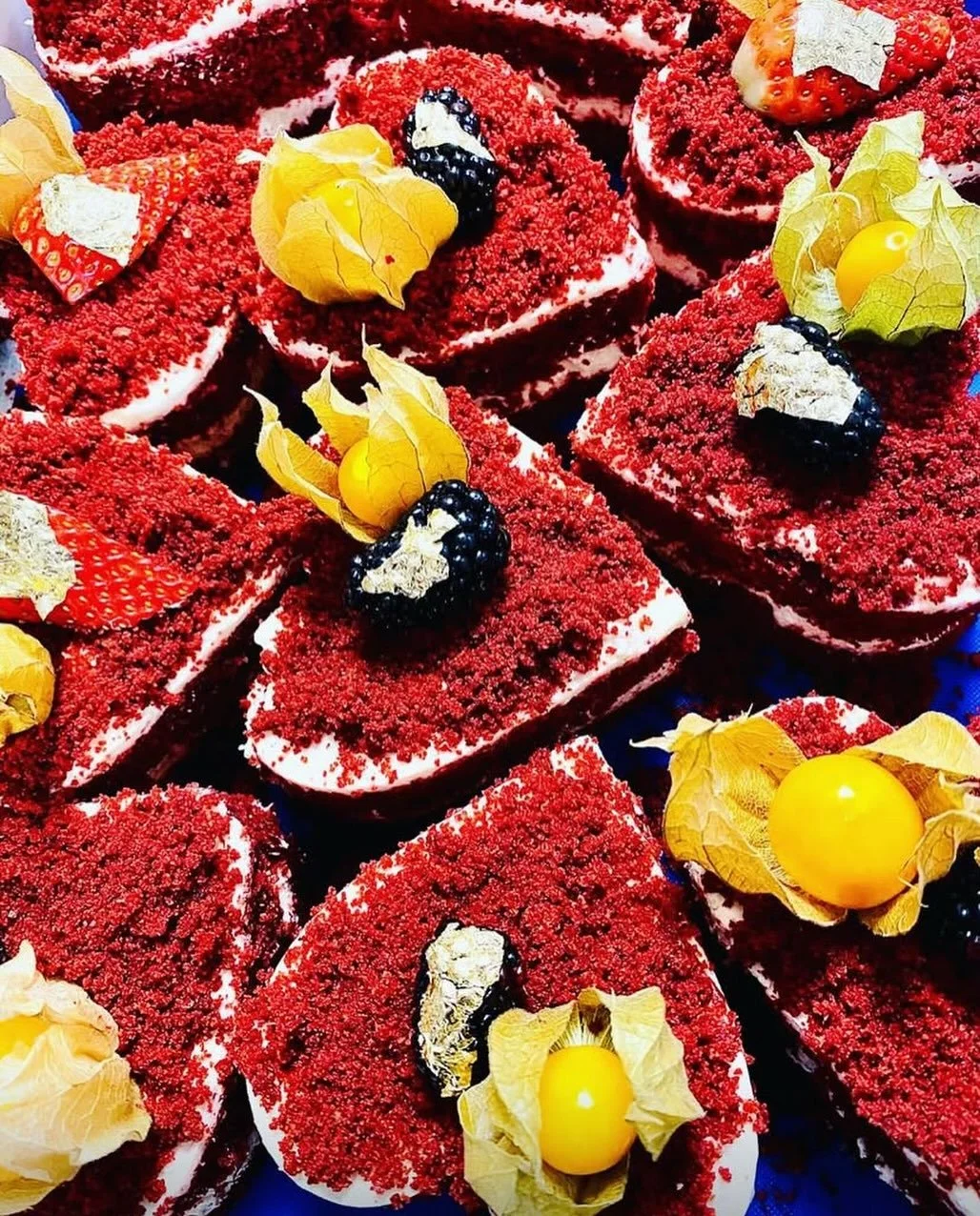 A close-up view of several slices of red velvet cake decorated with blackberries, strawberries, physalis, and edible gold leaf.