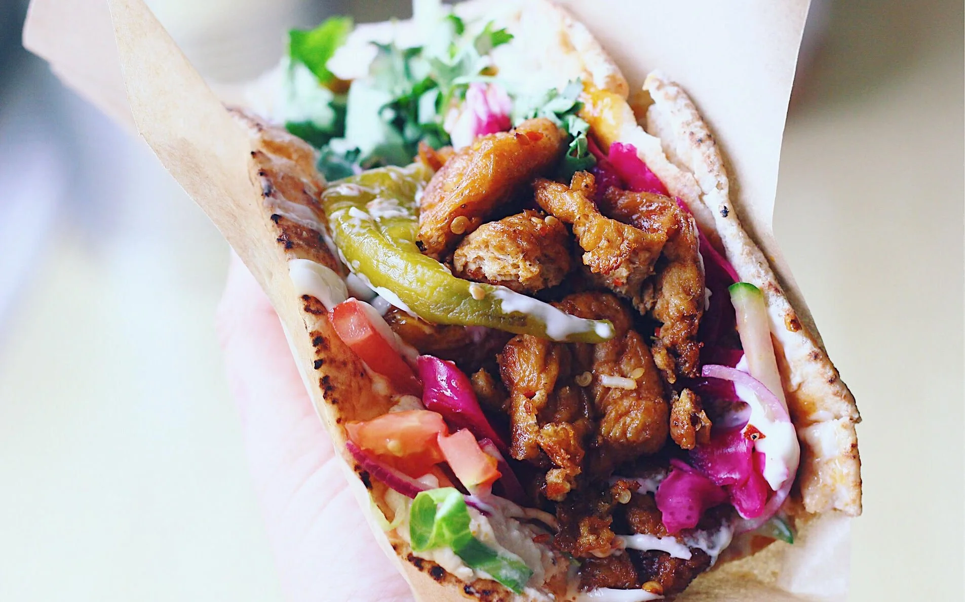A close-up view of a taco filled with seasoned meat, chopped tomatoes, shredded lettuce, pickled pink cabbage, creamy sauce, and a grilled tortilla shell.