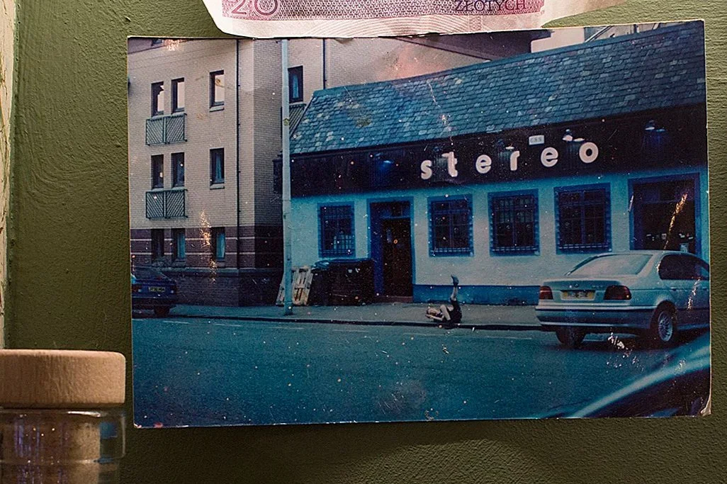 A photograph of a street scene showing a building with a sign that says 'stereo,' parked cars, and a scooter on the sidewalk.