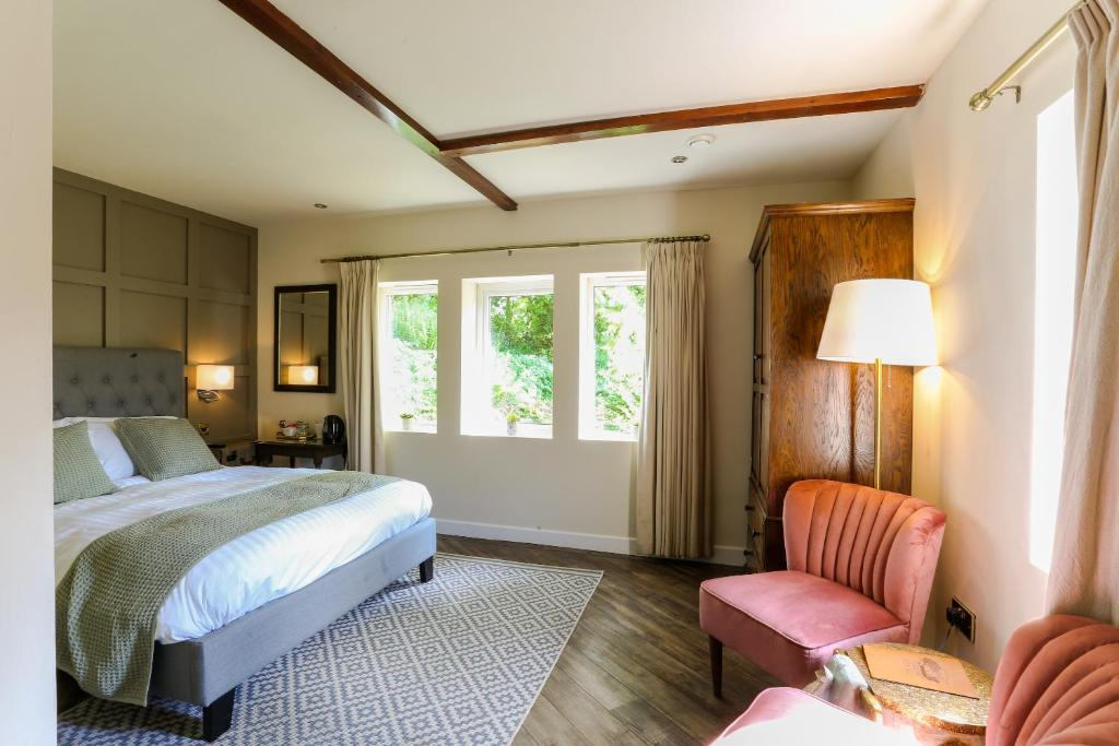 A cozy bedroom with a bed, pink velvet armchair, wooden cabinet, and a window with beige curtains.