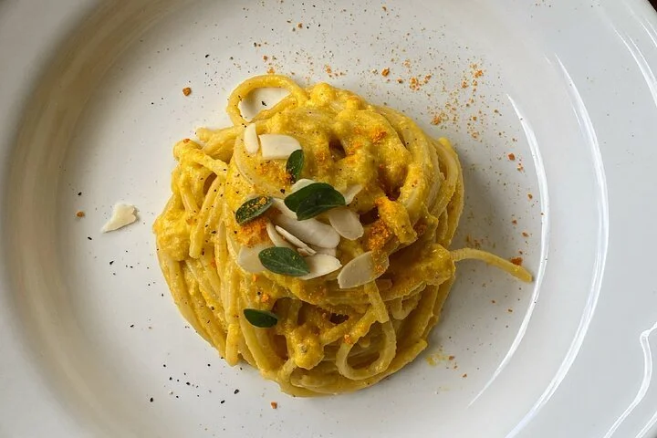 A plate of pasta with yellow sauce, topped with sliced almonds and fresh herbs.