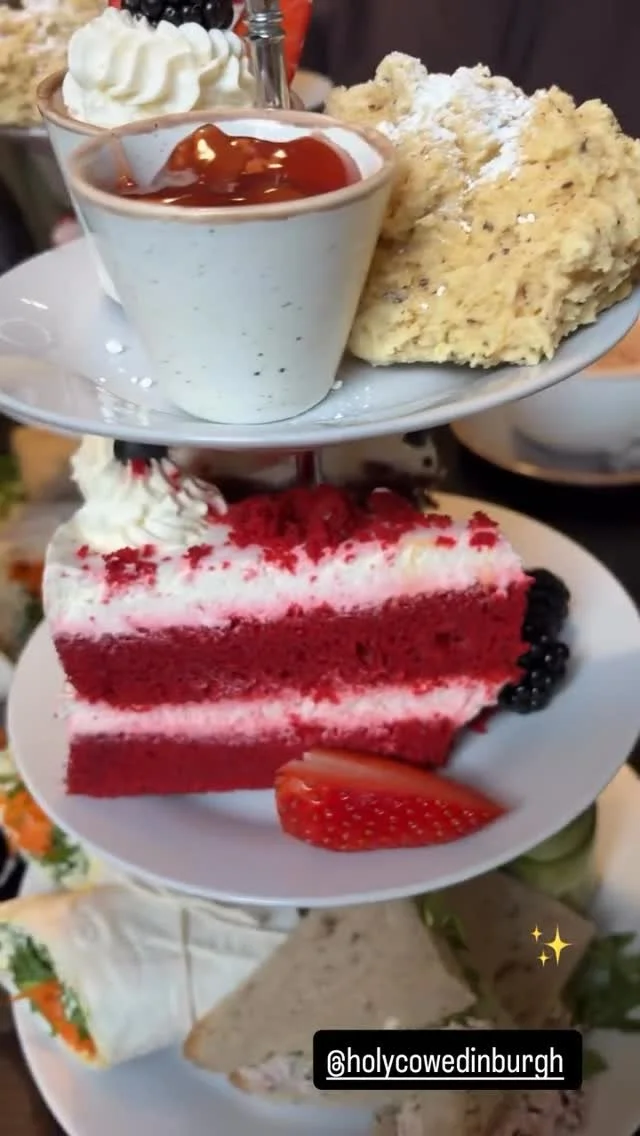A three-tiered dessert tray with whipped cream, a bowl of pudding topped with caramel sauce, a slice of red velvet cake with strawberries, and a sandwich with lettuce and turkey.