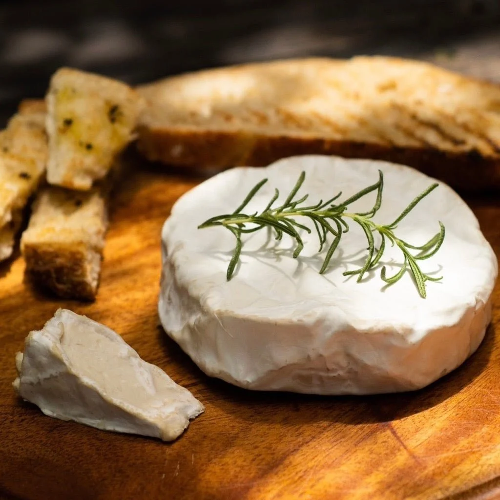 A wheel of brie cheese topped with a sprig of rosemary, served with toast points and crackers on a wooden cutting board.