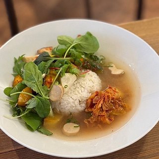 A bowl of soup with rice, shredded meat, vegetables, and greens.