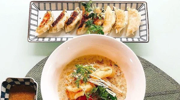 A bowl of Thai coconut curry with shrimp, garnished with herbs, and a plate of grilled or pan-fried dumplings with dipping sauce.
