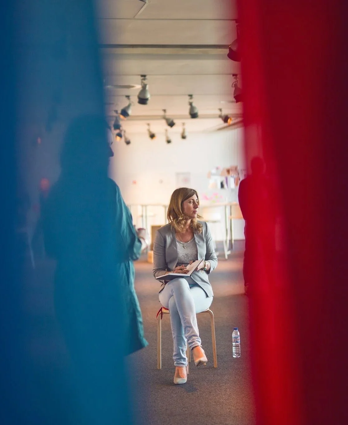 A THNK participant on a chair in a white room, seen between red and blue curtains