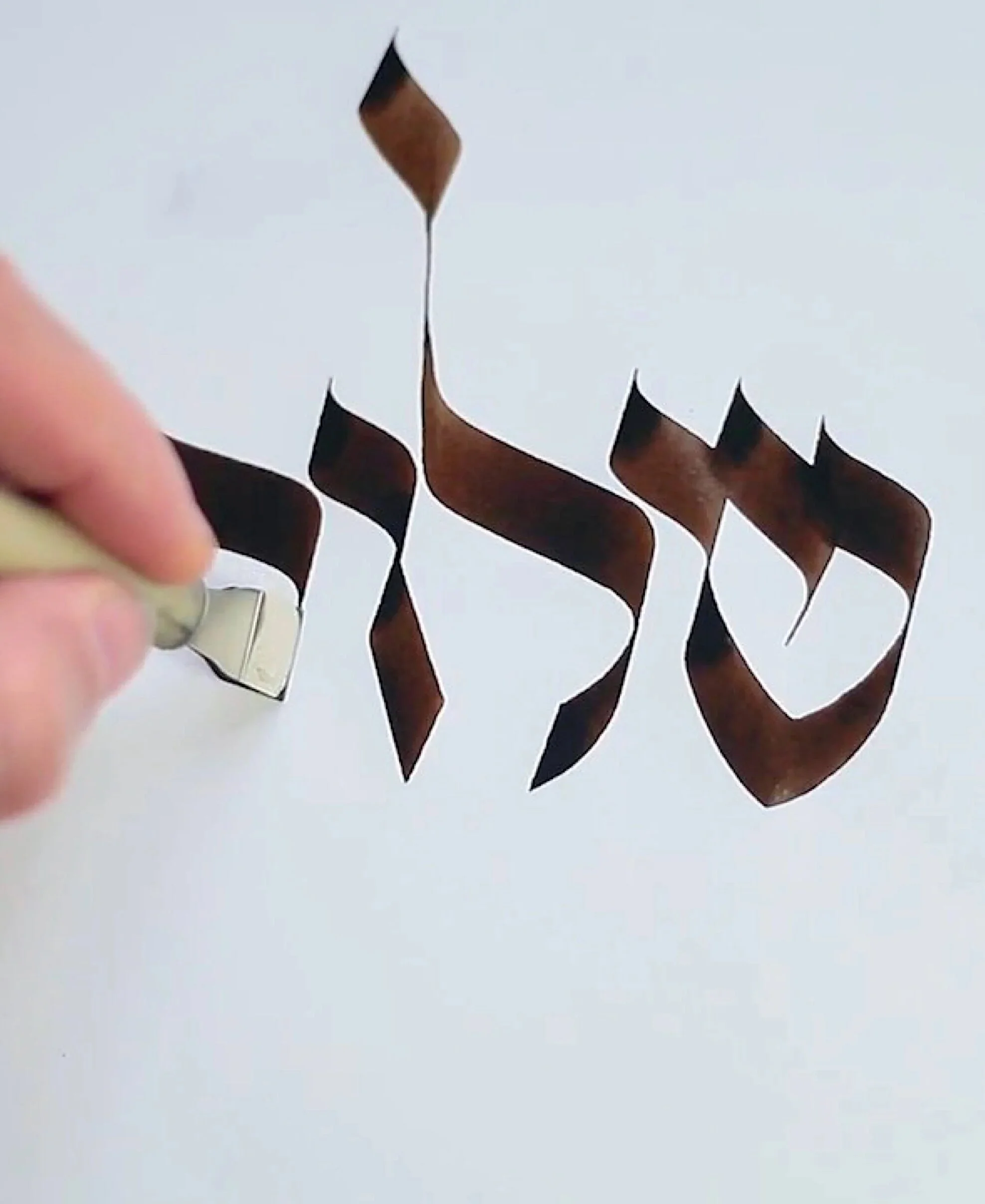 The Hebrew word shalom being written in brown ink with a calligraphy pen