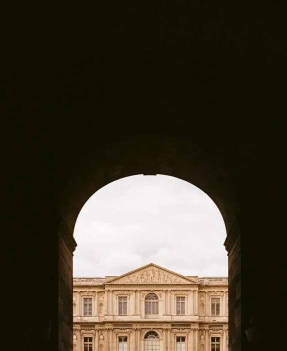 A Louvre facade framed by a dark stone archway in Paris