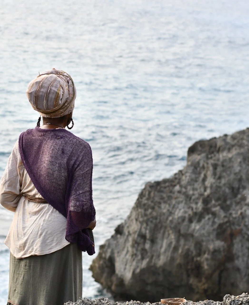 Marcia Douglas in a headwrap, looking out to sea from the rocks